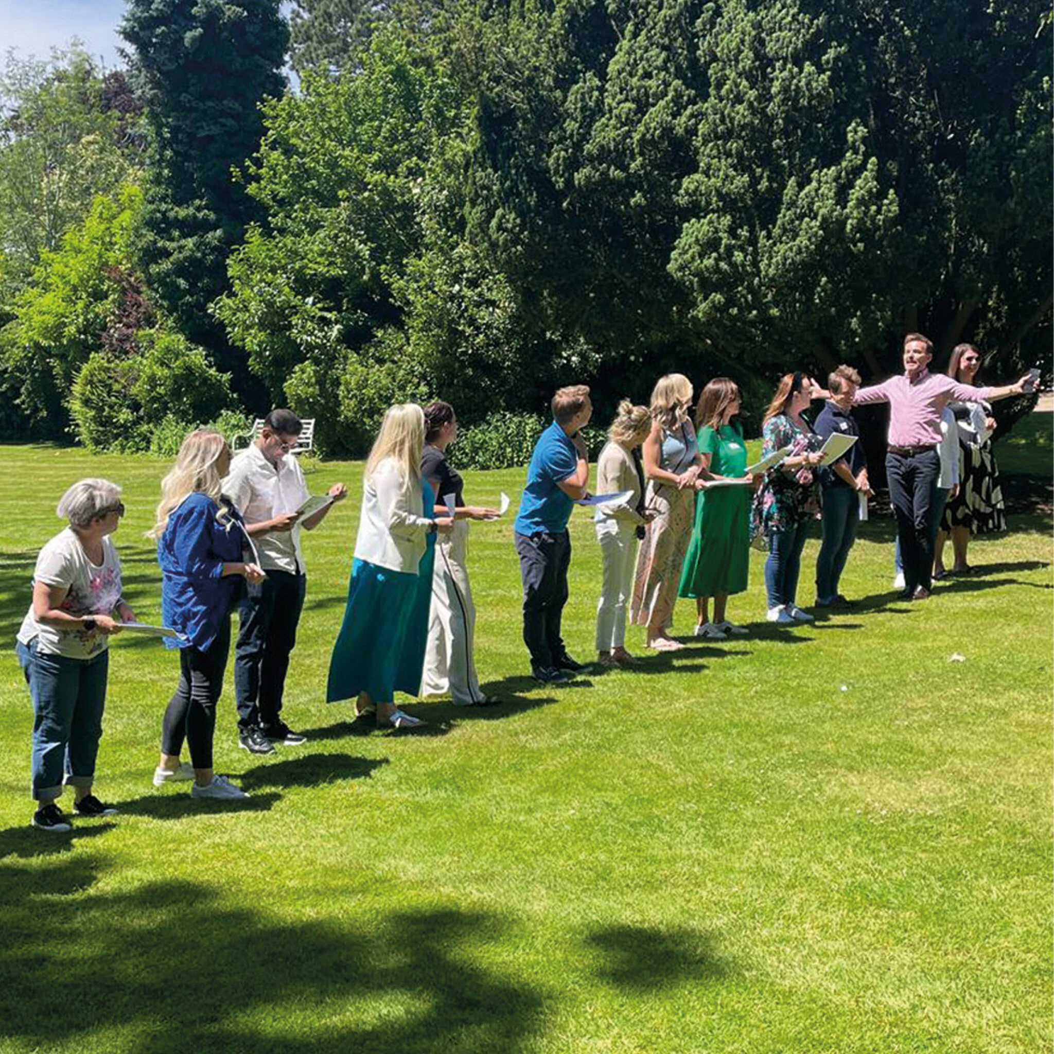 Group of Kallidus employees standing in a line on a lawn during an outdoor Insights Discovery activity, with Tim Jeary directing them.