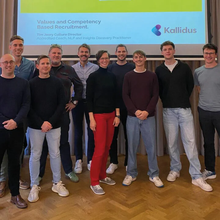 Group of Kallidus employees standing in front of a presentation screen showing Bowline branding and a workshop on values-based recruitment