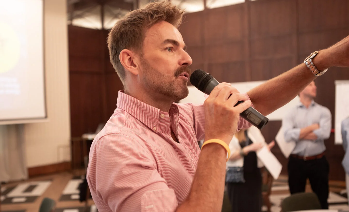Tim Jeary speaking into a microphone during a Kallidus Insights Discovery workshop, gesturing to a large group of employees.